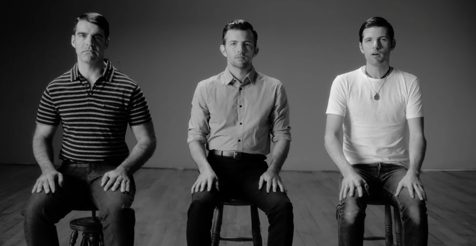 Three white men sit in chairs, facing front. The photo is in black and white.